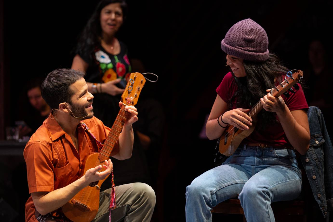 A man and a woman play stringed instruments as they smile at each other